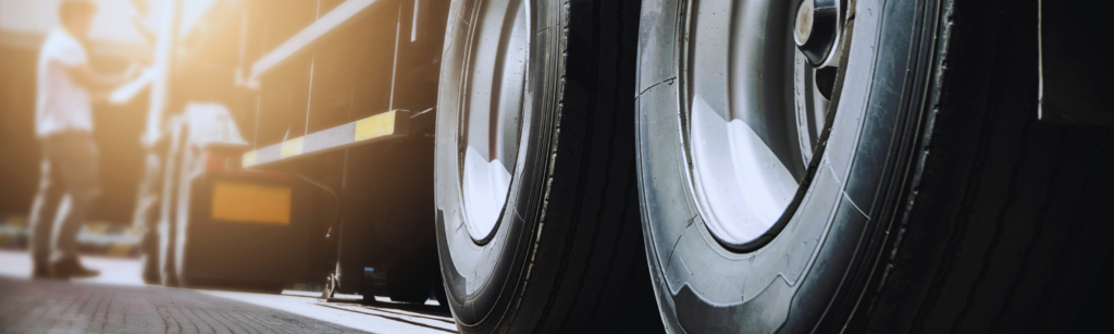 Close-up of large truck tires on a trailer with a blurred worker in the background at a loading dock