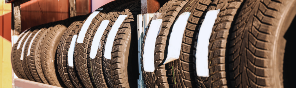 Rows of black car tires with white tag labels hanging in a tire shop display with warm lighting.